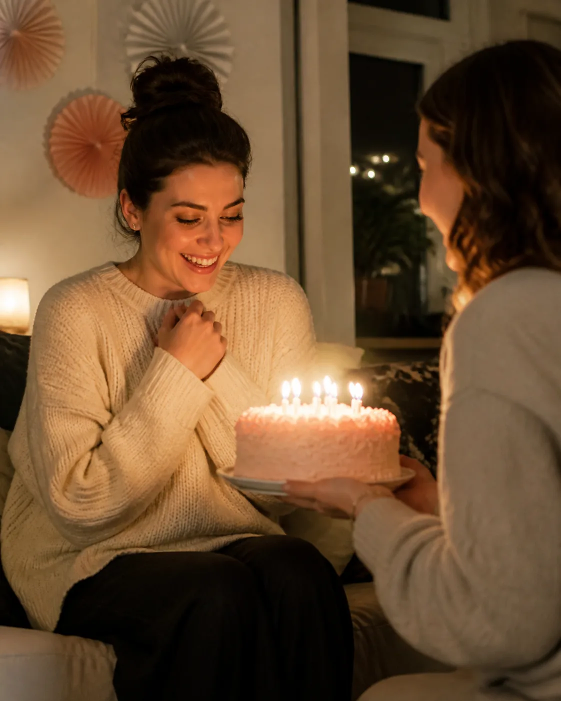 A fictional adult woman receiving a small birthday surprise in a cozy home, smiling toward a cake beside the sofa, warm lamps