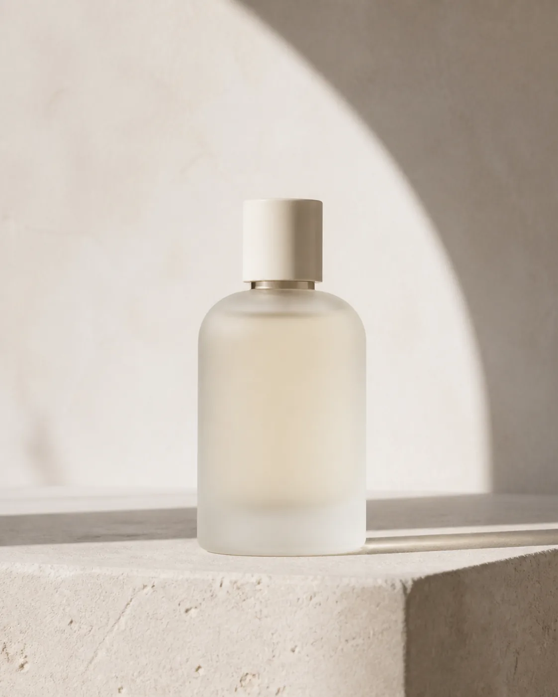 Minimalist product photograph of one unbranded frosted-glass fragrance bottle on white limestone, soft morning light with a f