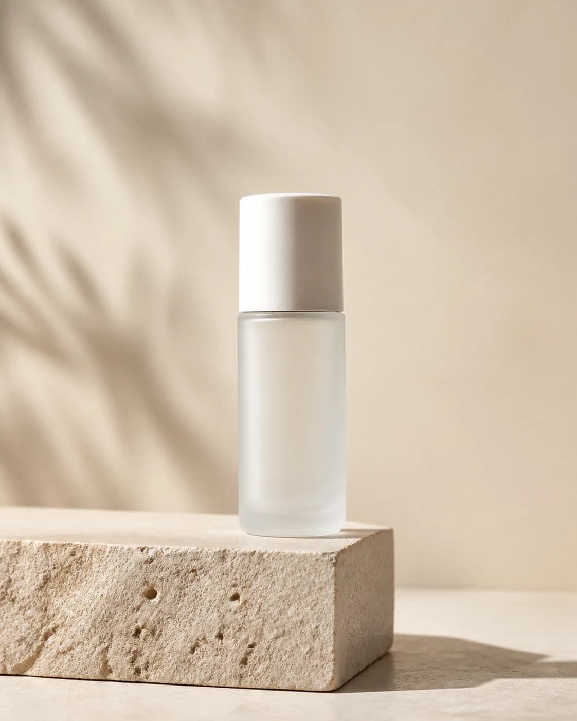 Minimalist product photograph of one unbranded frosted-glass skincare bottle with a plain white cap on a pale limestone block